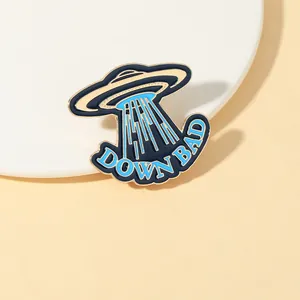 Detail of UFO enamel pin with 'DOWN BAD' text on a white circular display stand