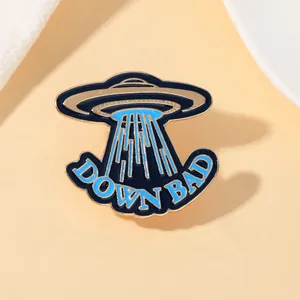 Macro detail of a blue UFO enamel pin with Down Bad text and golden plating