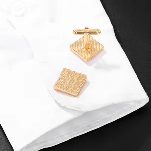 Mens gold square cufflinks with micro-grid texture on a white shirt cuff in close-up view