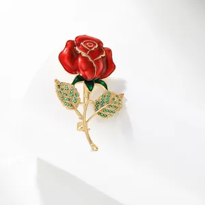Détail macro de broche rose émaillée rouge avec bords dorés et feuilles de cristal vert