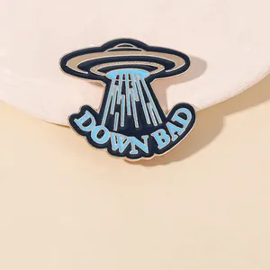 Macro shot of UFO enamel pin with 'DOWN BAD' text and blue polished finish detail