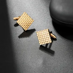 Detailed close-up of golden square cufflinks with grid texture on black matte background