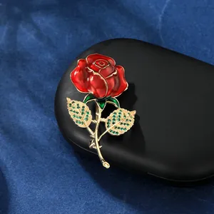 Vue macro d'une broche rose en émail rouge avec cristaux verts et tige dorée chic