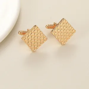 Close-up of square gold cufflinks with diamond grid pattern and metal texture details