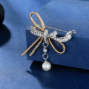 Macro detail of a bow-knot brooch with gold-silver tones, crystals, and a pearl drop