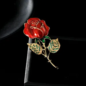 Détail d'une élégante broche rose en émail rouge avec feuilles de cristal vert et tige dorée