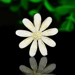 Macro di spilla a margherita in smalto bianco con bordo dorato su sfondo nero lucido