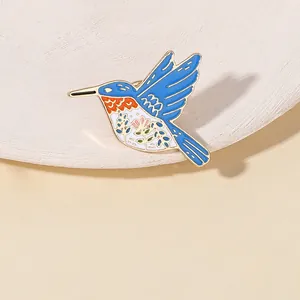 Detailed close-up of a hummingbird enamel brooch with blue wings and colorful flower patterns