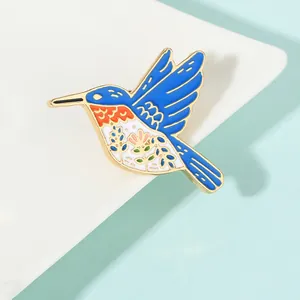 Macro detail of enamel hummingbird brooch with vibrant blue wings and floral belly pattern
