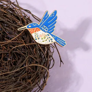 Macro detail of enamel hummingbird brooch with vibrant blue wings on a nest branch
