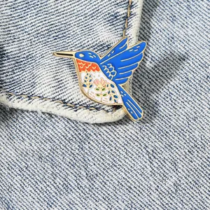 Exquisite hummingbird enamel brooch featuring vibrant blue and orange floral feather details