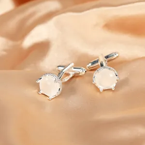 Dettaglio di gemelli a corona in argento con pietre su sfondo di seta champagne