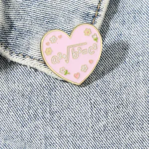 Pink heart enamel brooch with mathematical formula on denim fabric background