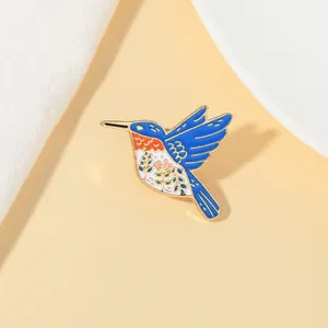 Detail of colorful enamel hummingbird brooch with intricate floral patterns on gold metal