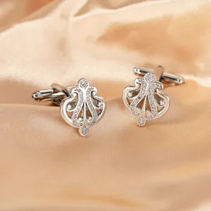 Detail of silver crown cufflinks with micro-set zircons on champagne satin background