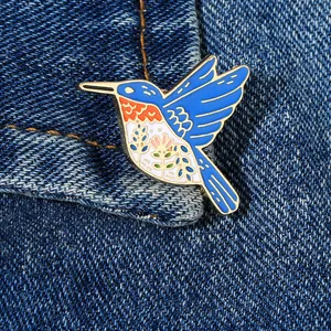 Macro shot of colorful enamel hummingbird brooch with floral paint on blue denim jacket