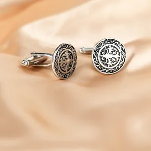 Macro shot of silver cufflinks with embossed tree patterns on champagne silk background