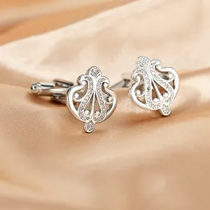 Detailed macro view of silver crown cufflinks with crystals on champagne silk fabric