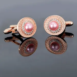 Dettaglio dei gemelli in oro rosa con perla rosa e corona di cristalli lucenti su fondo scuro