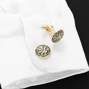 Details runder gold-schwarzer Manschettenknöpfe mit Retro-Muster an weißem Hemd