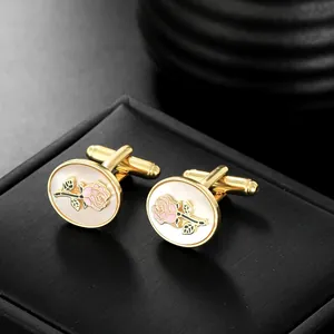 Close-up of golden rose cufflinks with white pearl inlay on black textured jewelry box