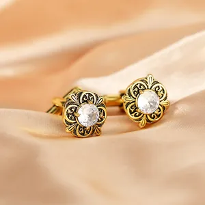 Close-up of golden vintage cufflinks with hollow floral design and central white crystal