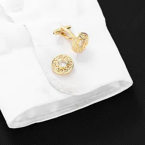 Detailed close-up of golden hollow cufflinks with center crystal on a white shirt cuff