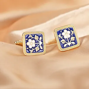Detail of square gold cufflinks with blue enamel and white floral motifs on silk fabric