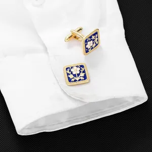 Detail of square gold cufflinks with blue enamel floral pattern on white shirt cuff