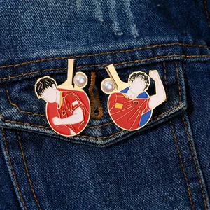 Detail of red enamel table tennis brooches with pearls on blue denim fabric