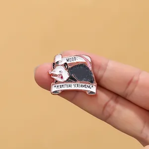 Gros plan sur le pin's opossum en émail avec texte Mood Perpetual Screaming doré