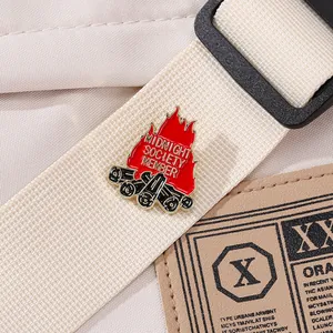 Detail of Midnight Society enamel pin with campfire design on beige canvas strap