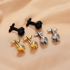 Macro shot of twisted metal cufflinks in black, gold, and silver on silk background