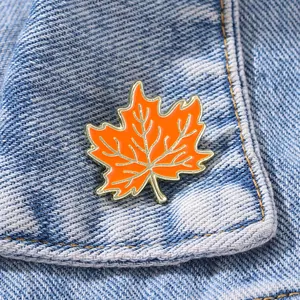 Broche feuille d'érable en émail orange et bordure dorée sur tissu en jean bleu