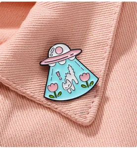 Gros plan d'une broche chat OVNI en émail épinglée sur un col de chemise rose