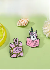 Detail von rosa Einhorn- und Kaninchen-Buch-Emaille-Pins auf dekorativem grünem Hintergrund