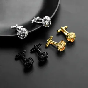 Macro shot of silver, gold, and black silk knot metal cufflinks on a textured surface