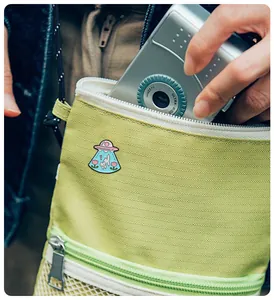 Détail d'un pin's chat OVNI en émail sur un sac vert avec un appareil photo vintage
