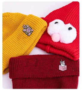 Nahaufnahme von rosa Einhorn- und Buchnadeln auf bunten groben Strickmützen