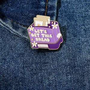 Macro shot of purple enamel bread pin with Let's Get This Bread text on denim