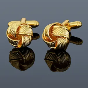 Close-up of golden knot cufflinks with textured engraving on a reflective surface