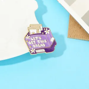 Detail of purple enamel bread basket brooch with 'LET'S GET THIS BREAD' slogan on blue background