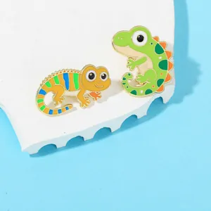 Detail of two colorful enamel lizard brooches with gold plating on a textured white stone
