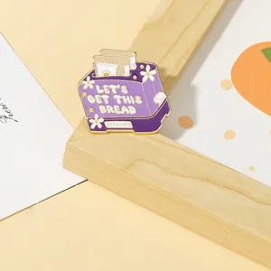 Detail of purple toaster enamel pin with Let's Get This Bread slogan and floral design