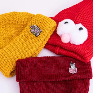 Drei Strickmützen in Gelb, Rot und Burgund mit süßen Einhorn- und Monster-Abzeichen