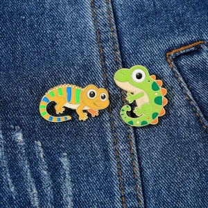 Detail of two colorful lizard enamel pins on denim fabric showing fine alloy craftsmanship