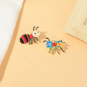 Detail of cute bee and ant enamel pins on a warm orange background with elegant wooden frame