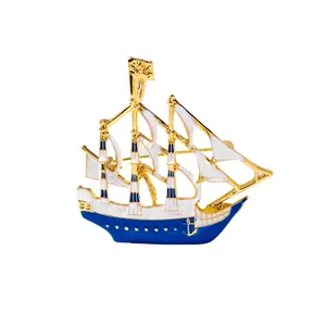 Golden sailboat enamel brooch pin with white sails and navy blue hull on white backdrop