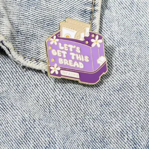 Detail of purple toaster enamel pin with slogan on light blue denim fabric