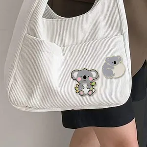 Set di due simpatiche spille smaltate a forma di koala su una borsa tote in velluto